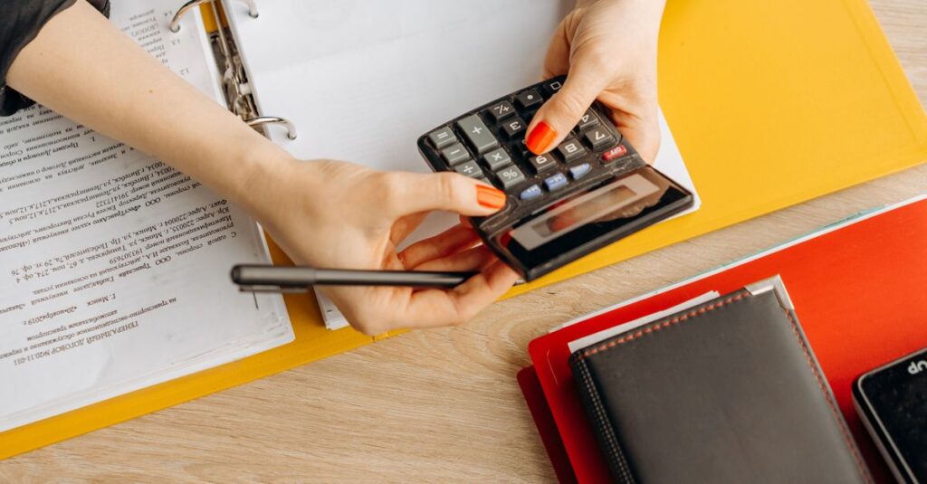 Hands using a calculator over financial documents and folders
